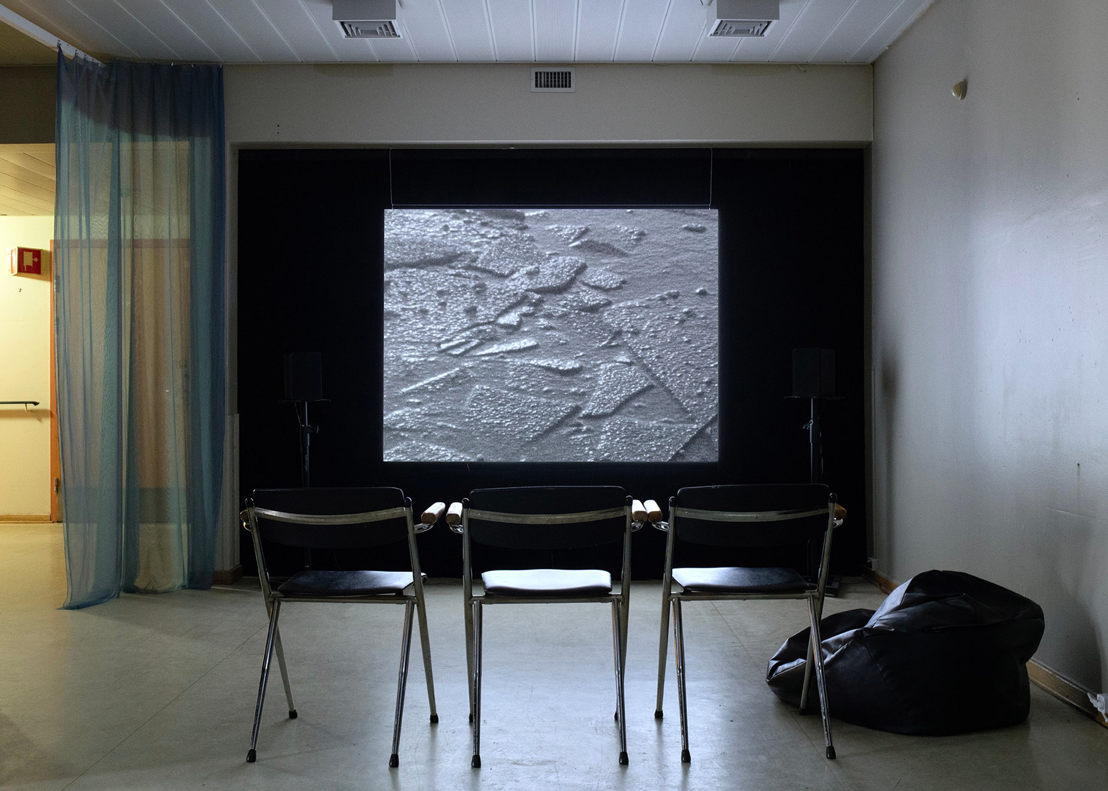 Chairs stand in front of a projections screen with a blue curtain hung to the left