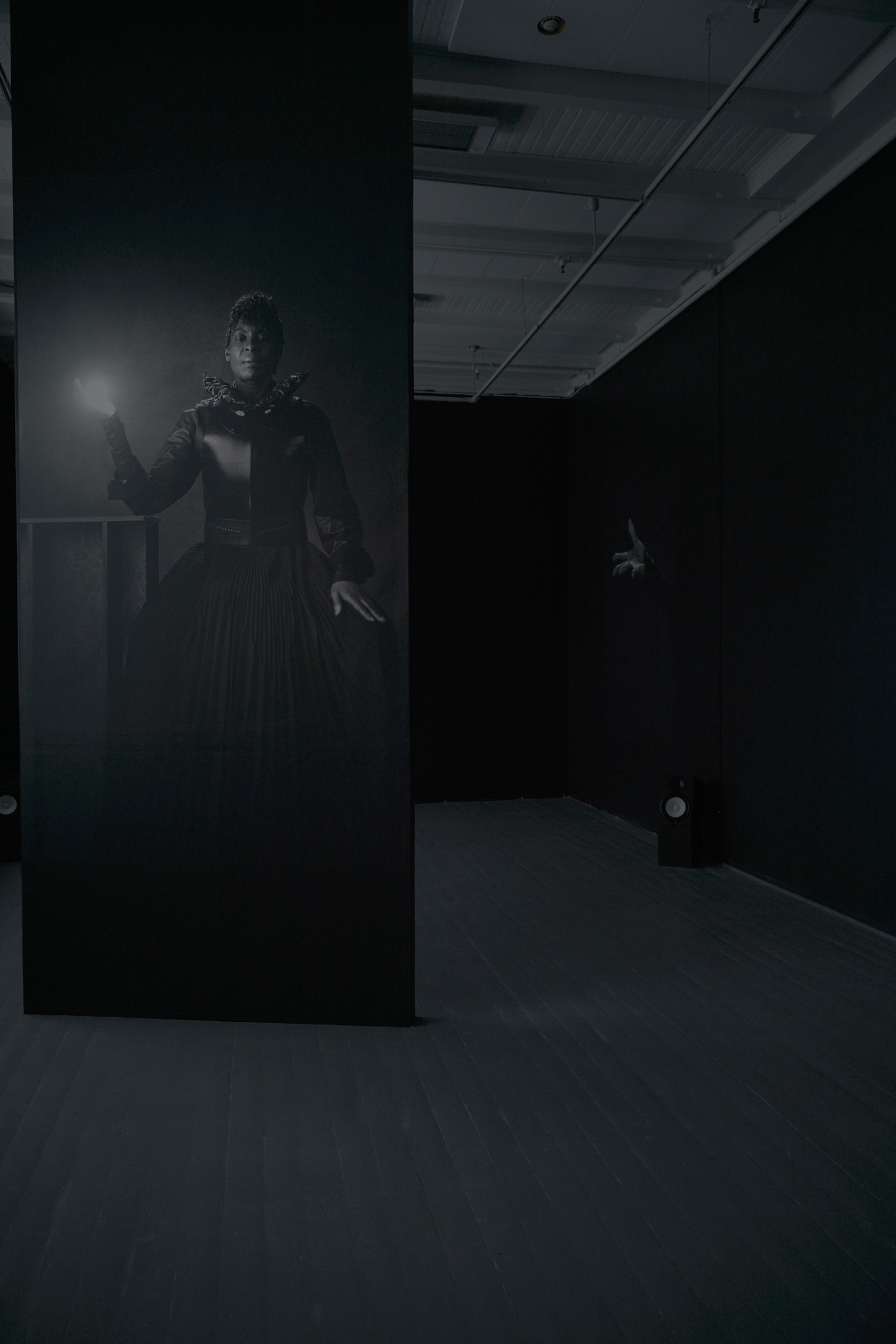 En dame i en svart kjole som holderen lyskule blir projisert på en svart vegg, i et svart rom.