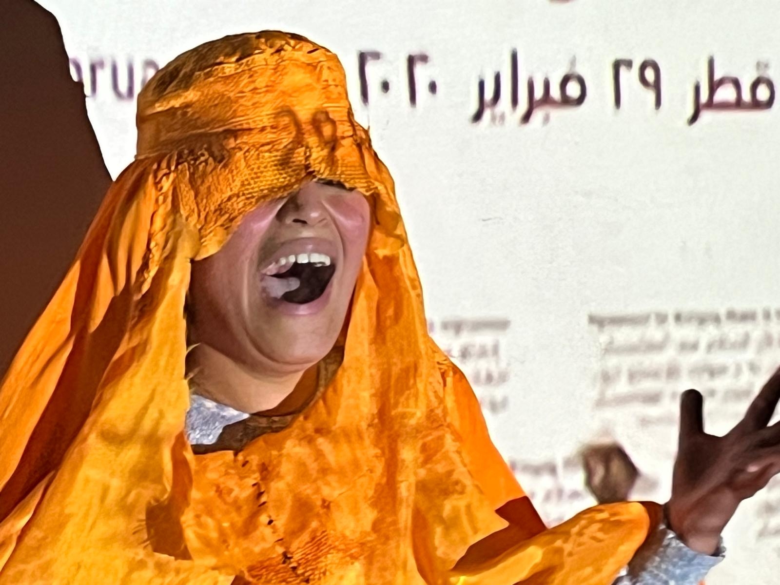 A woman's face screams under an orange veil which covers head, eyes and shoulders.