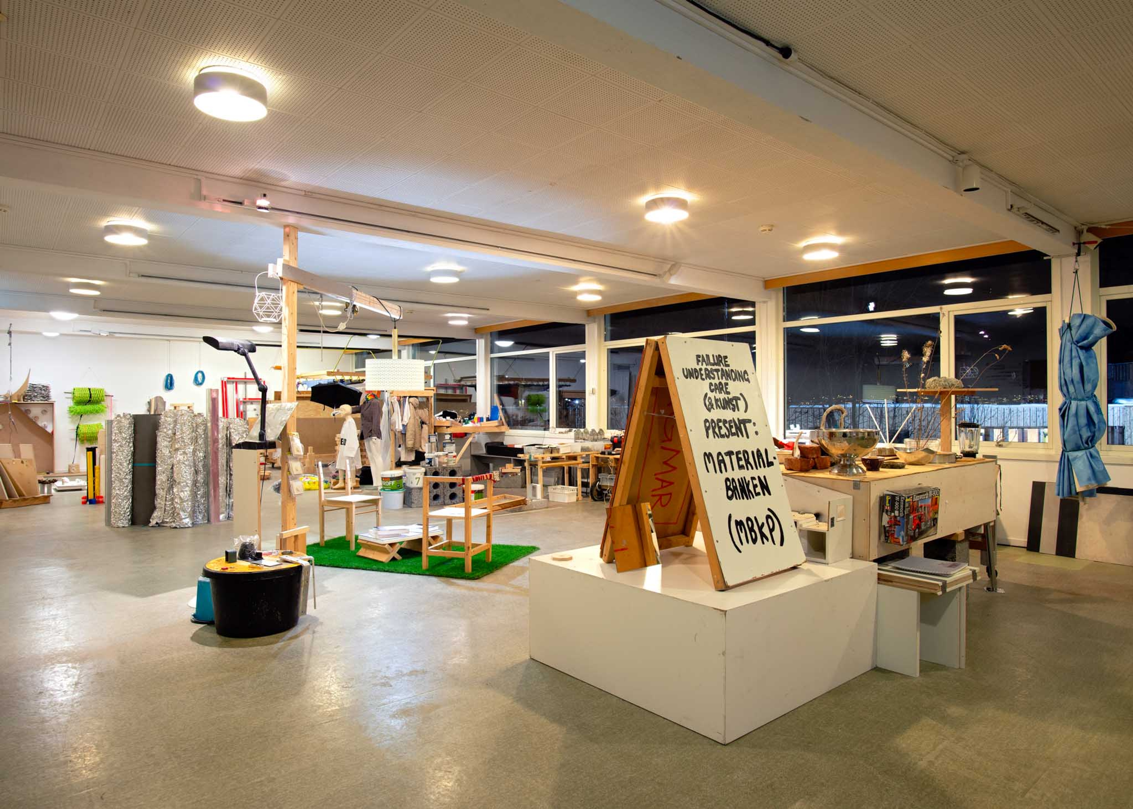 A large room filled with various objects. A poster board reads 'Material banken'.