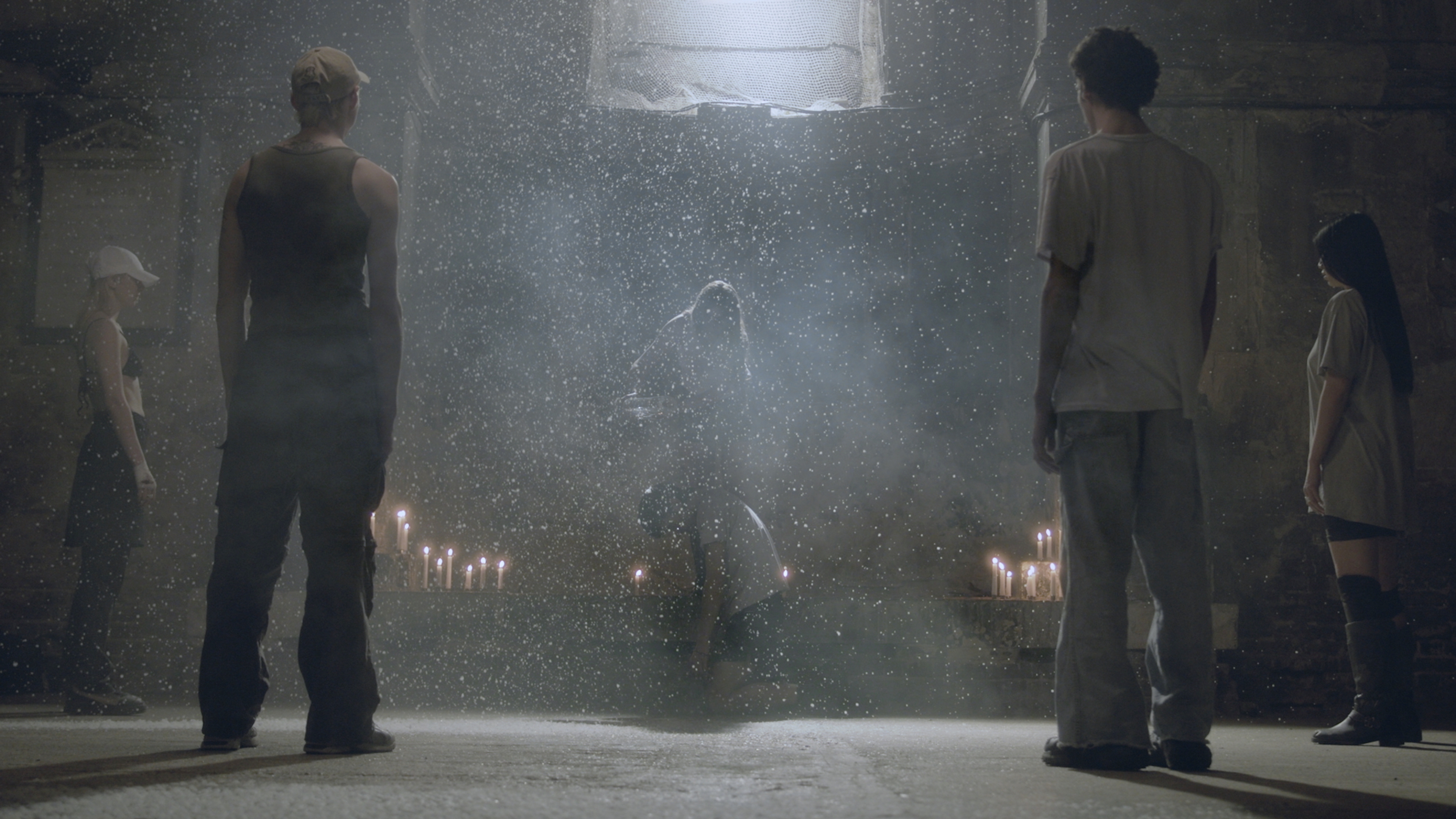 People stand in a circle around candles and a person in the middle surrounded by dust