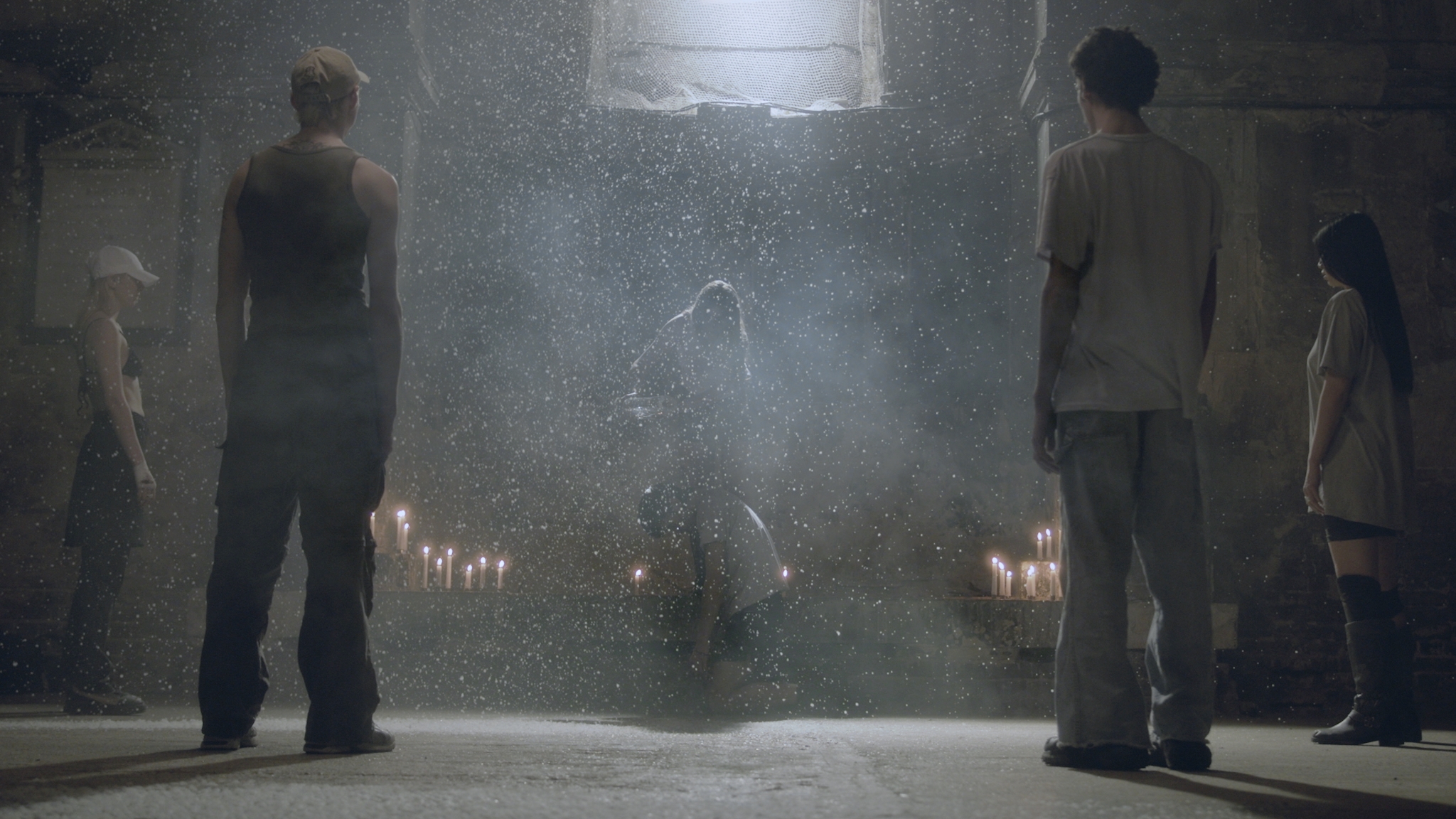 People stand in a circle around candles and a person in the middle surrounded by dust