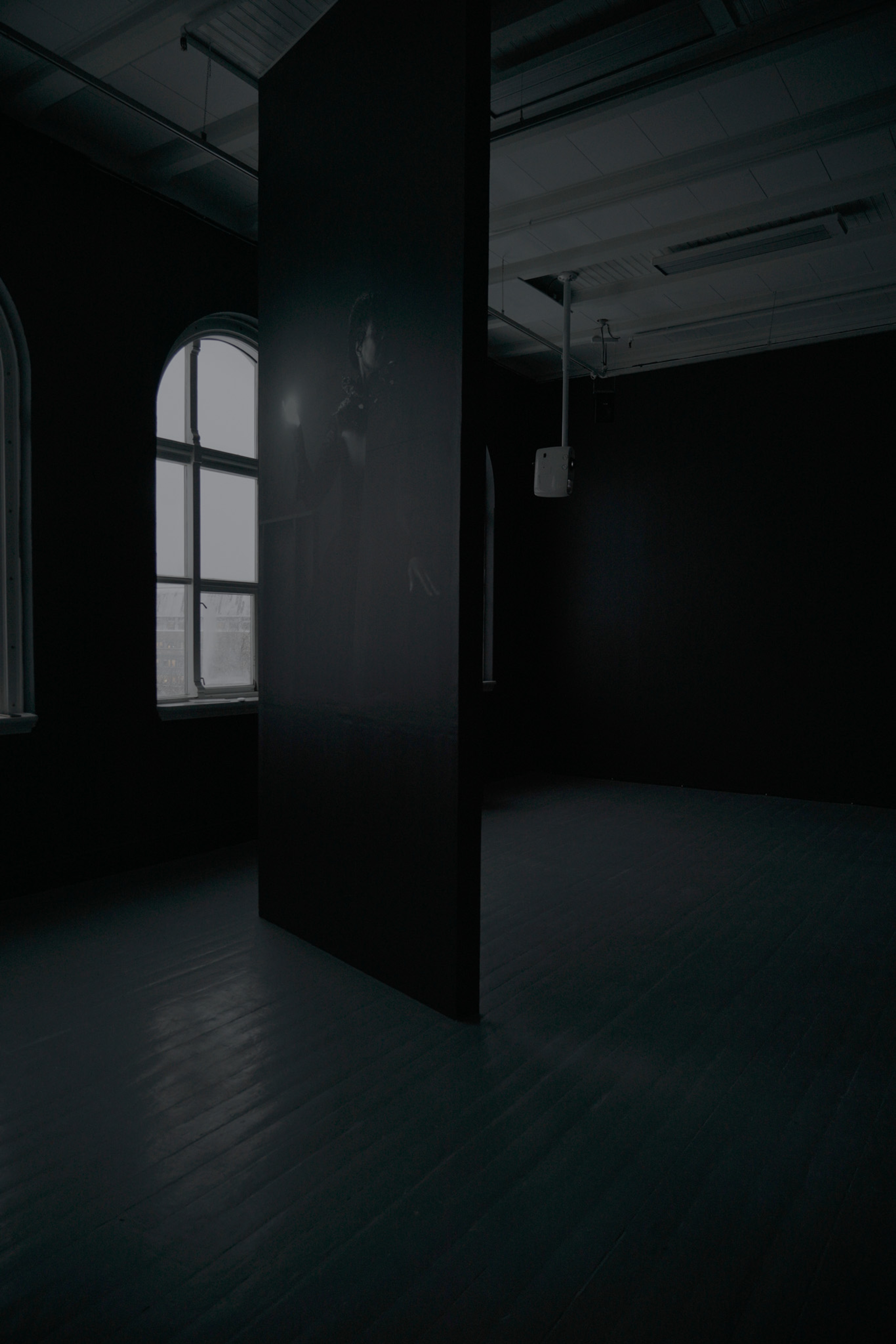 Et vertikalt panel fra gulv til tak viser en kvinne som holder en lyskule foran et vindu