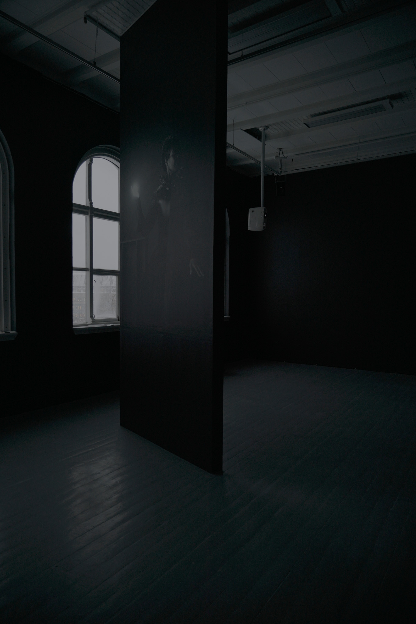 Et vertikalt panel fra gulv til tak viser en kvinne som holder en lyskule foran et vindu