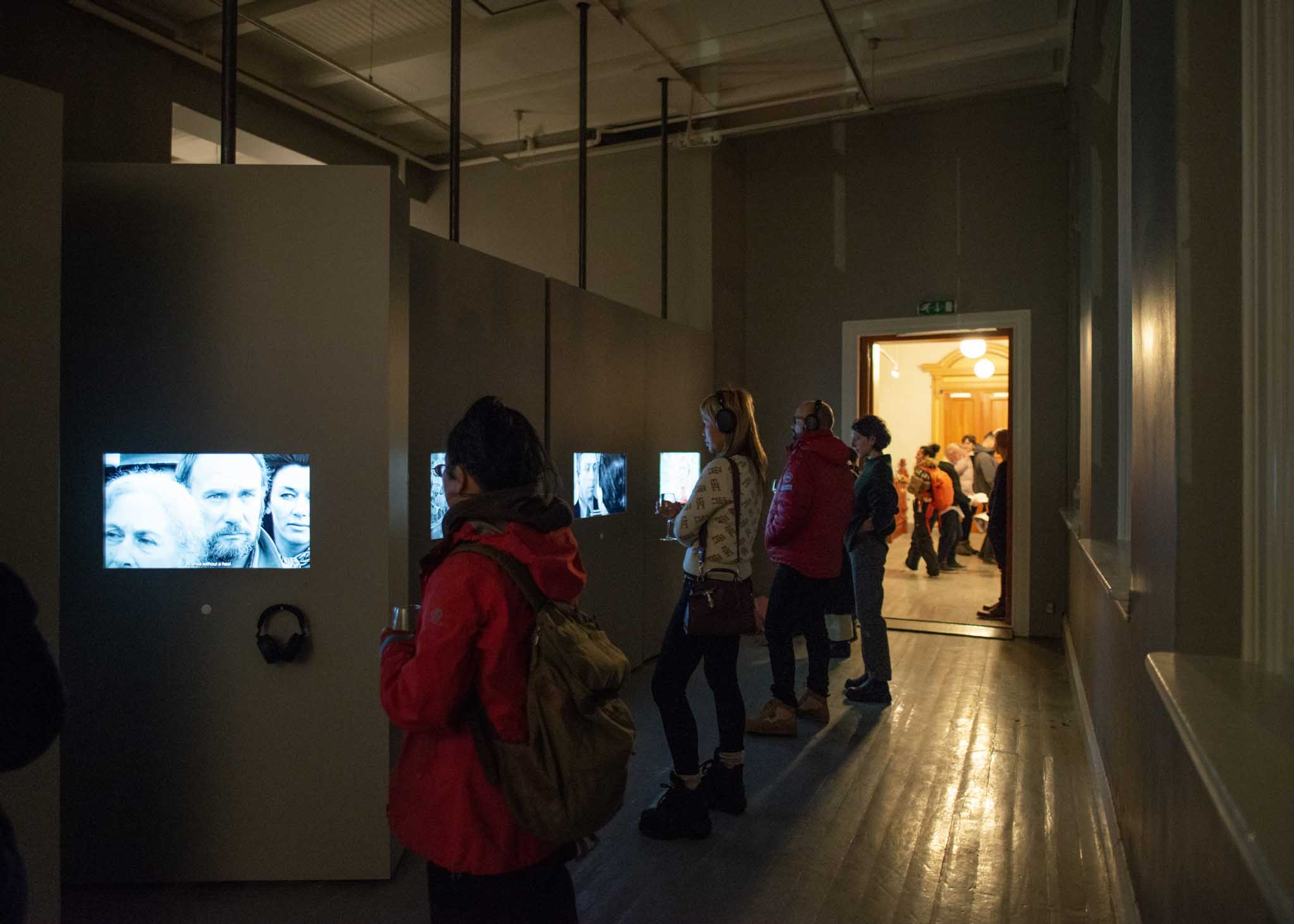 Lots of people watch different TV screens in a busy gallery.