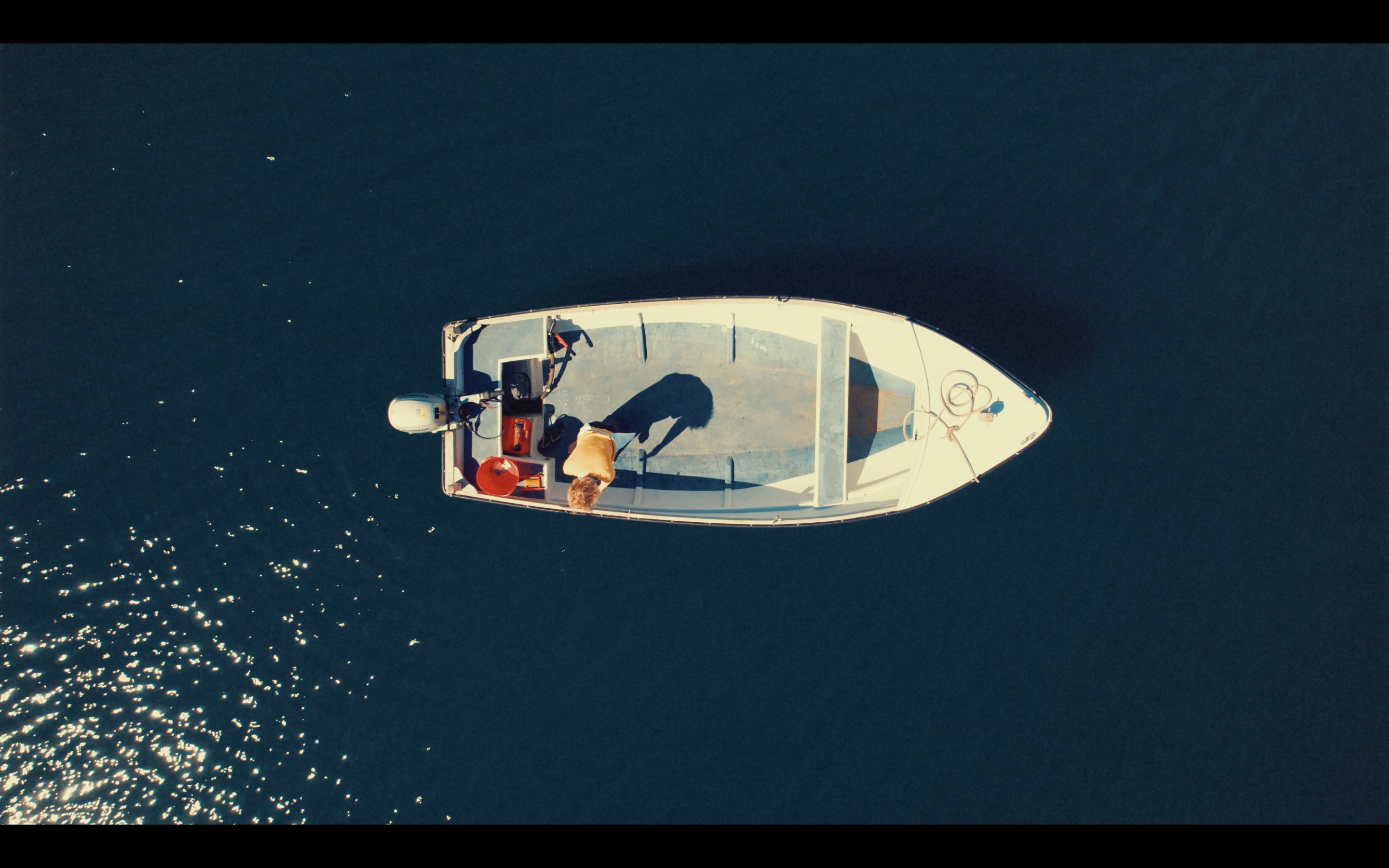 A white motor boat is seen from above, static in a deep blue sea.