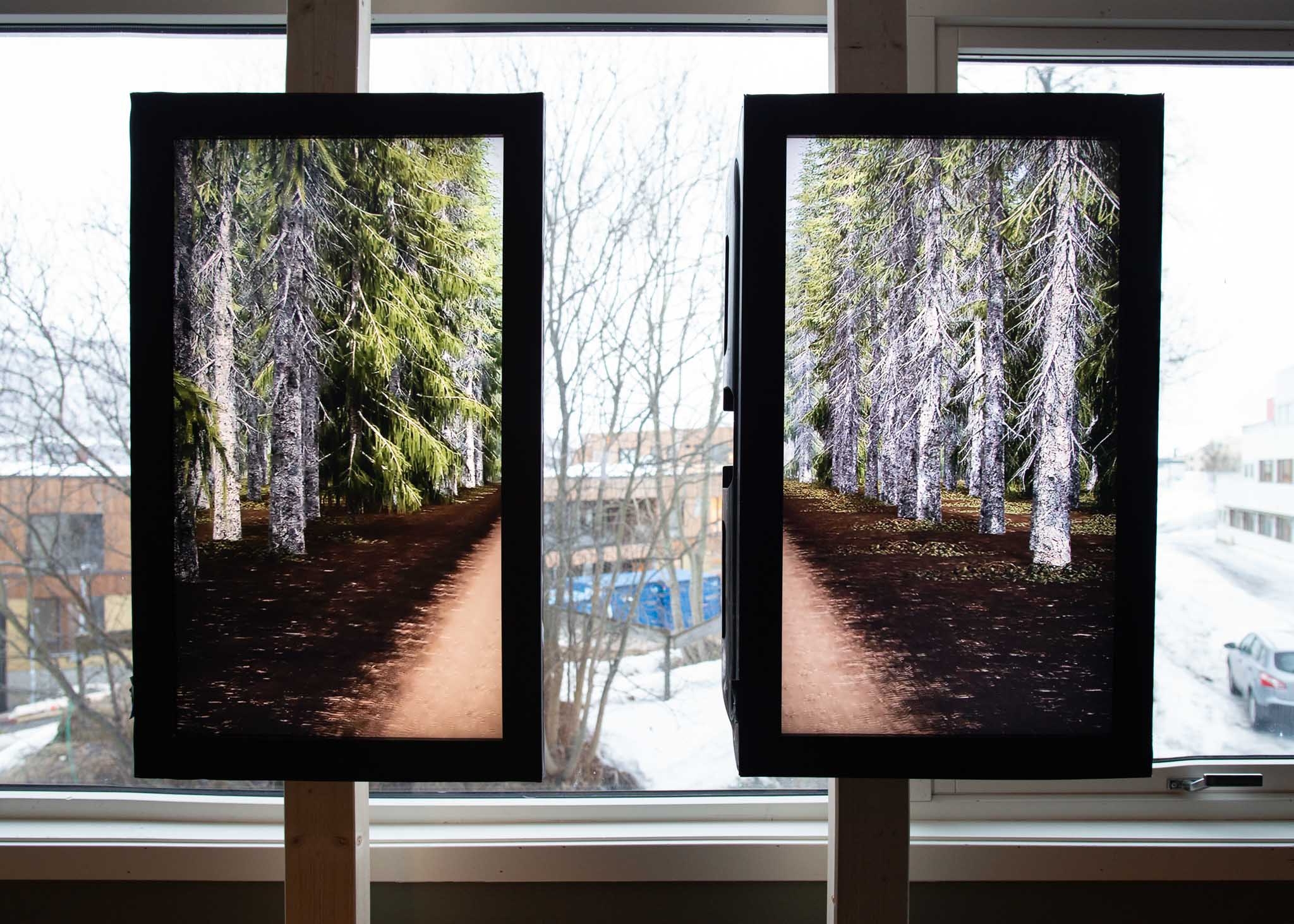 Two screens mounted vertically in front of a window, each showing one half of the film.