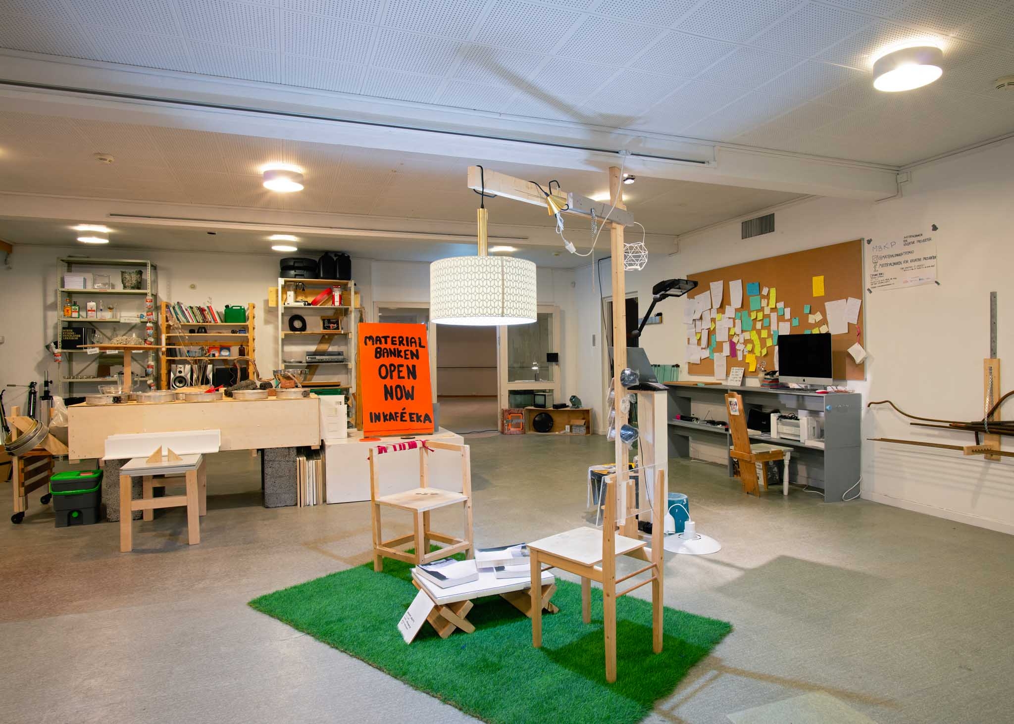 Two DIY chairs stand under a wooden lamp on artificial grass. Random objects are displayed in the background.