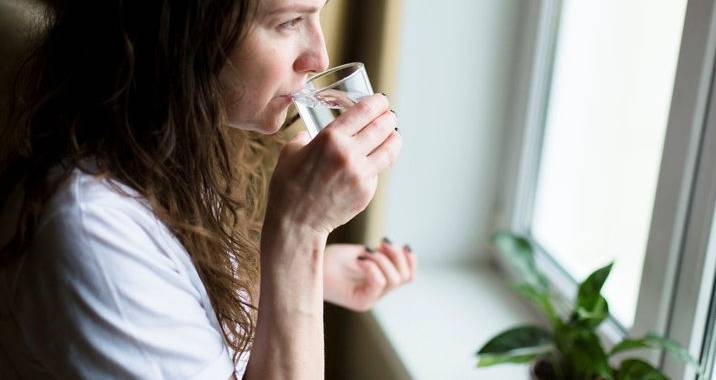 Dame drikker et glass vann mens hun ser ut av vinduet