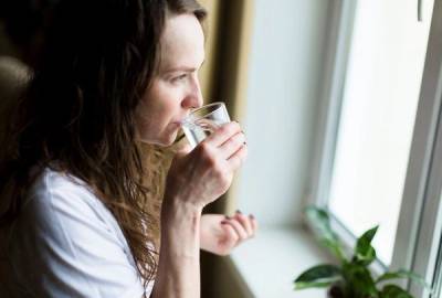 Dame drikker et glass vann mens hun ser ut av vinduet