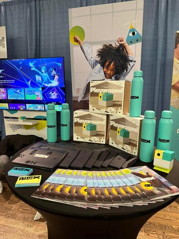 Product display table featuring Nex Playground boxes and branded water bottles at Pepcom NYC.