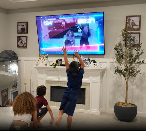 Three children actively playing the Laser Dodge game in their living room, with one boy jumping up to avoid a virtual laser on the television connected to the Nex Playground console.