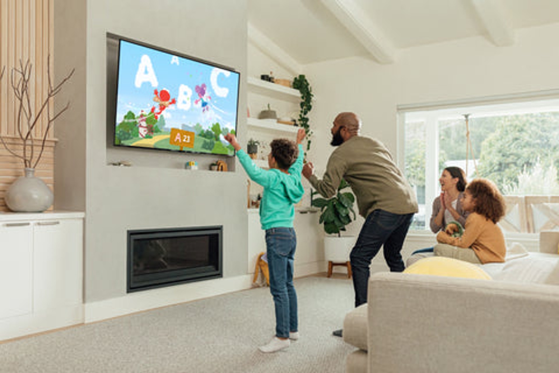 A family enjoying an active educational video game in their living room, with a father and son reaching up to catch virtual alphabet letters alongside Elmo on the Nex Playground console.