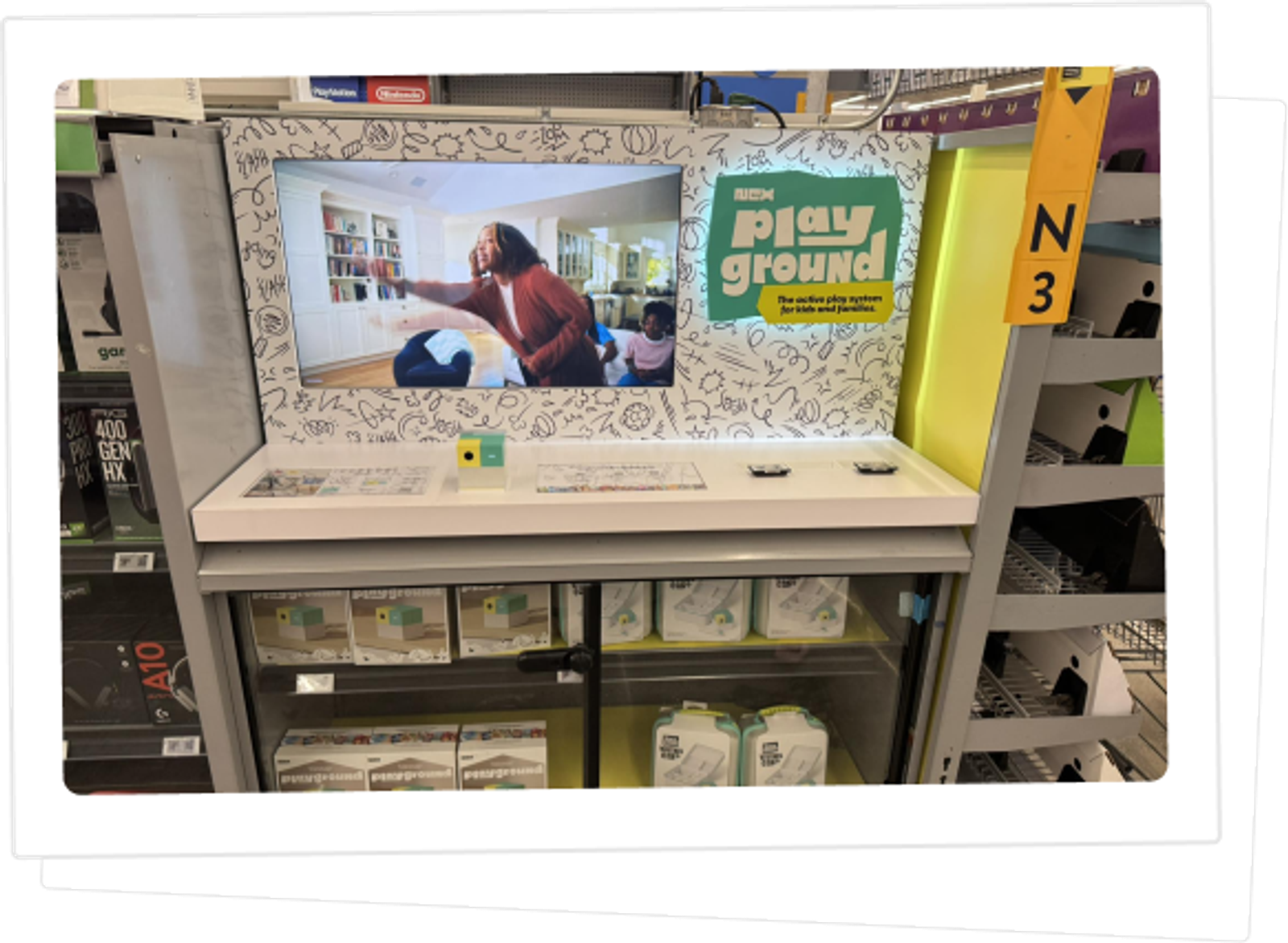 A Nex Playground retail display in a store aisle, with boxed consoles on the shelf below.