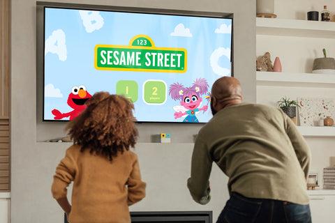 A father and daughter playing an interactive Sesame Street educational game on a television connected to the Nex Playground console.