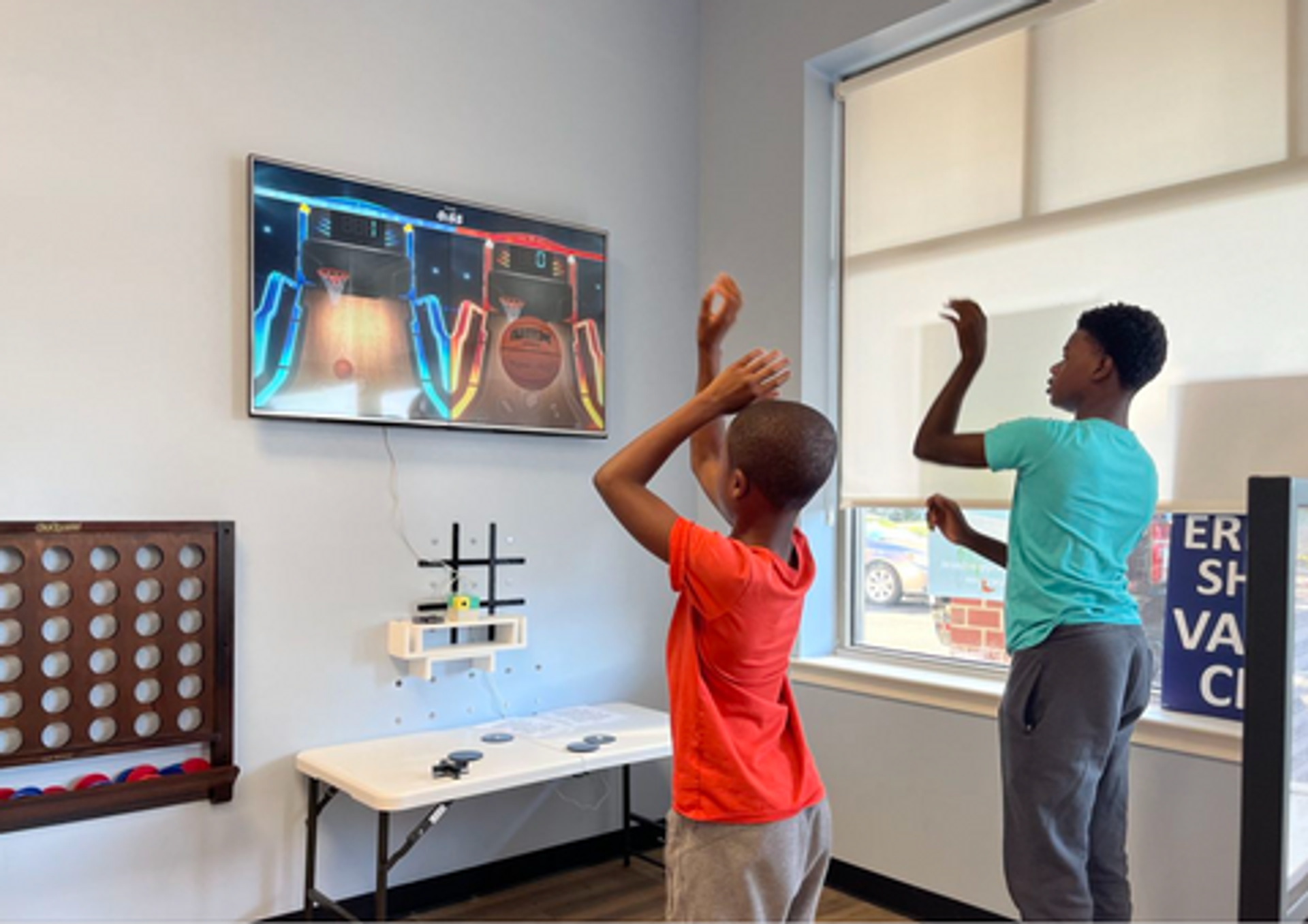 Two boys playing the Basketball Knockout active game on the Nex Playground console in the waiting room of the Eric's RX community vaccine clinic.