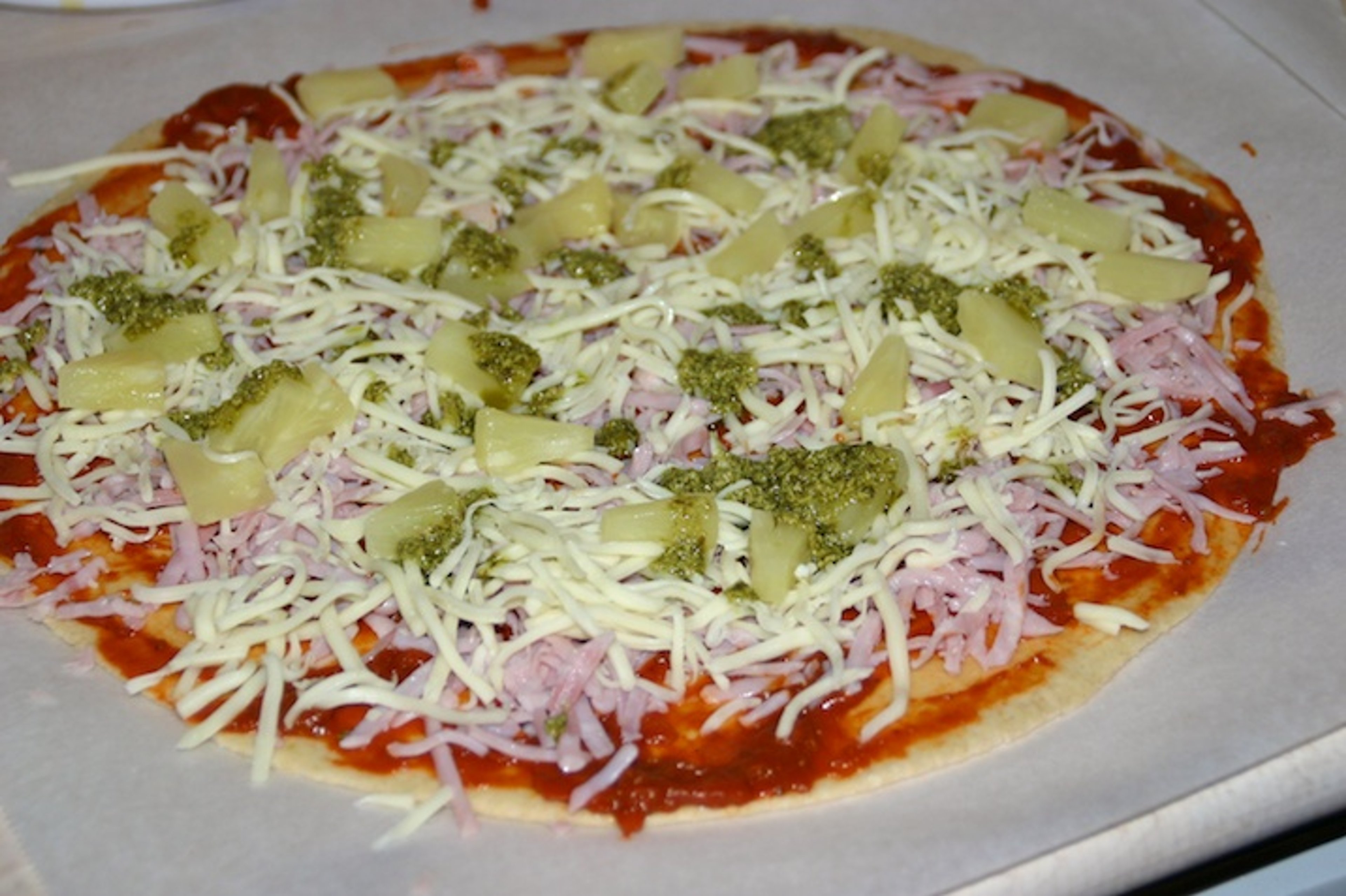 Pizza med fuldkornsbund, tomatsauce, ost, skinke, ananas og pesto