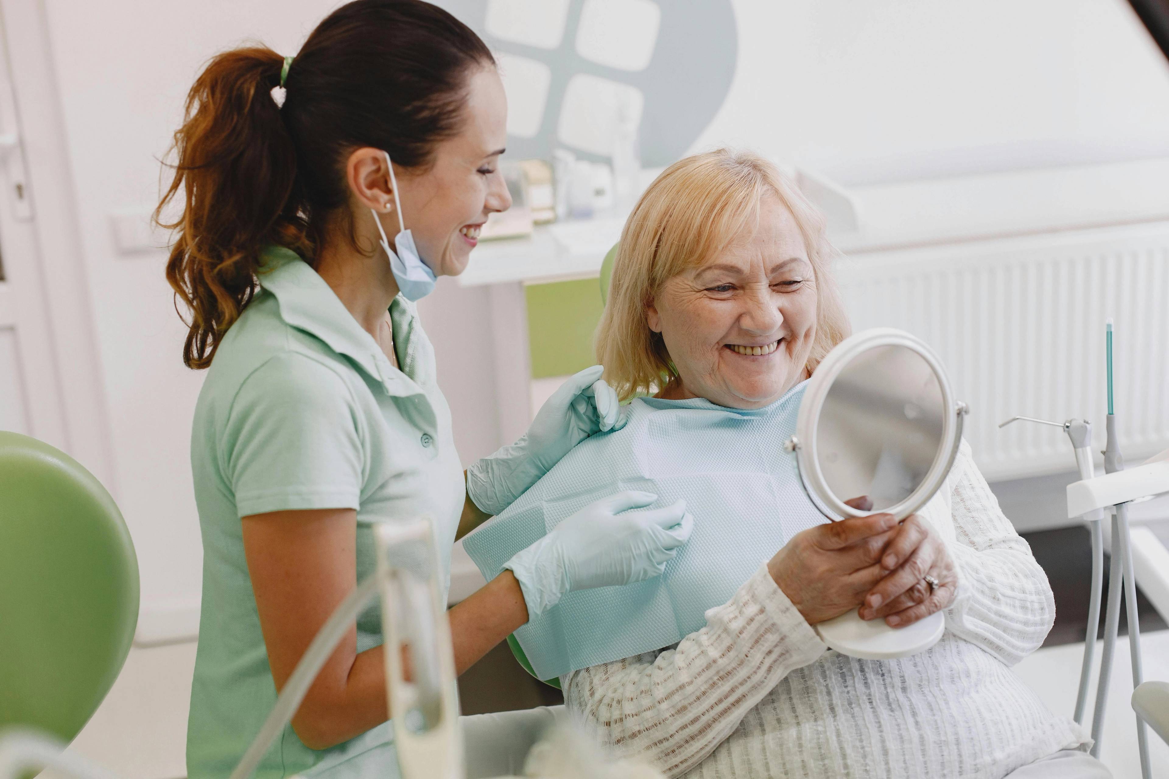 An older female patient smiles as she looks at herself in a hand mirror