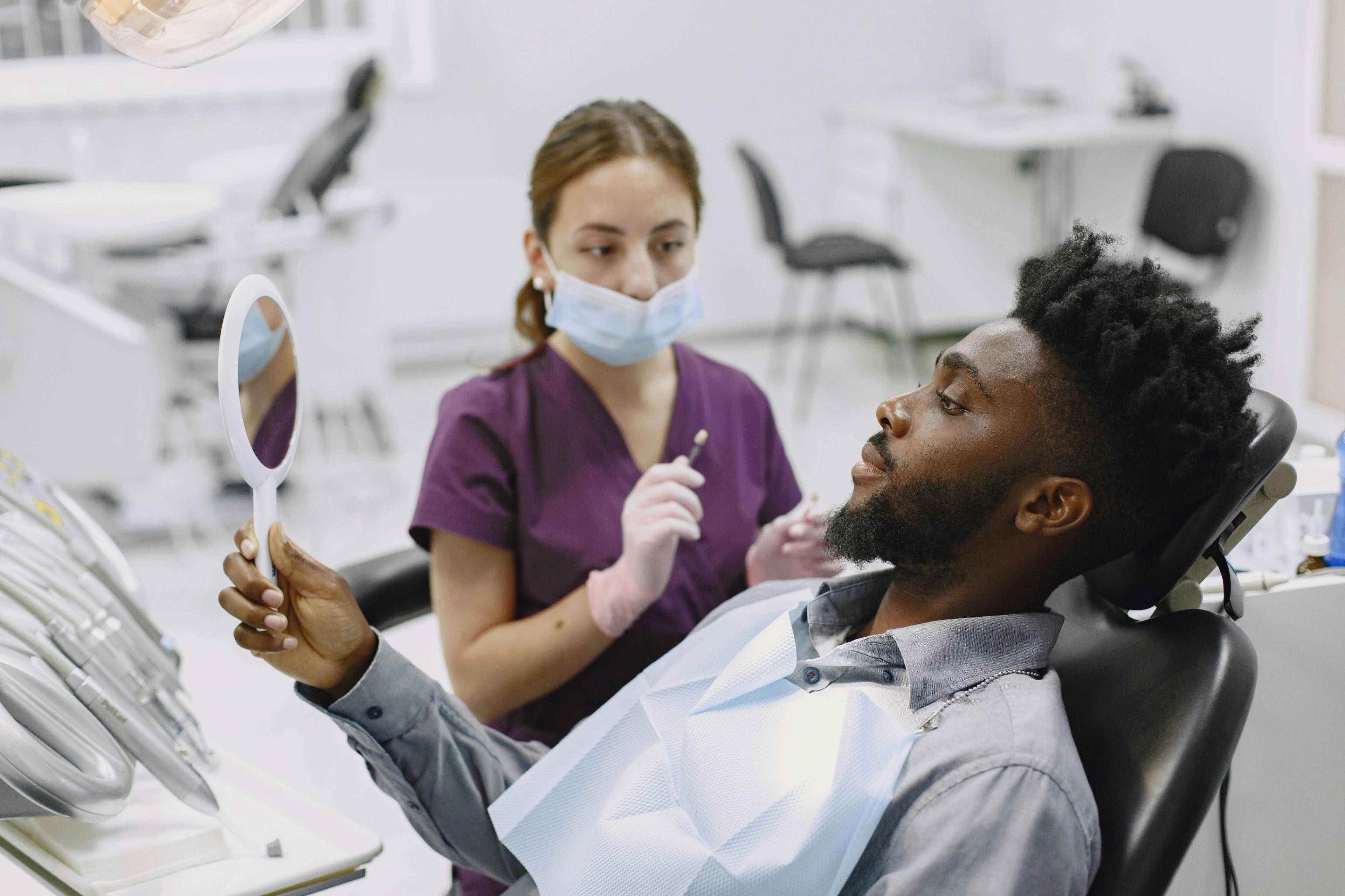 A stock photo of a patient holding a hand mirror in a dental treatment chair