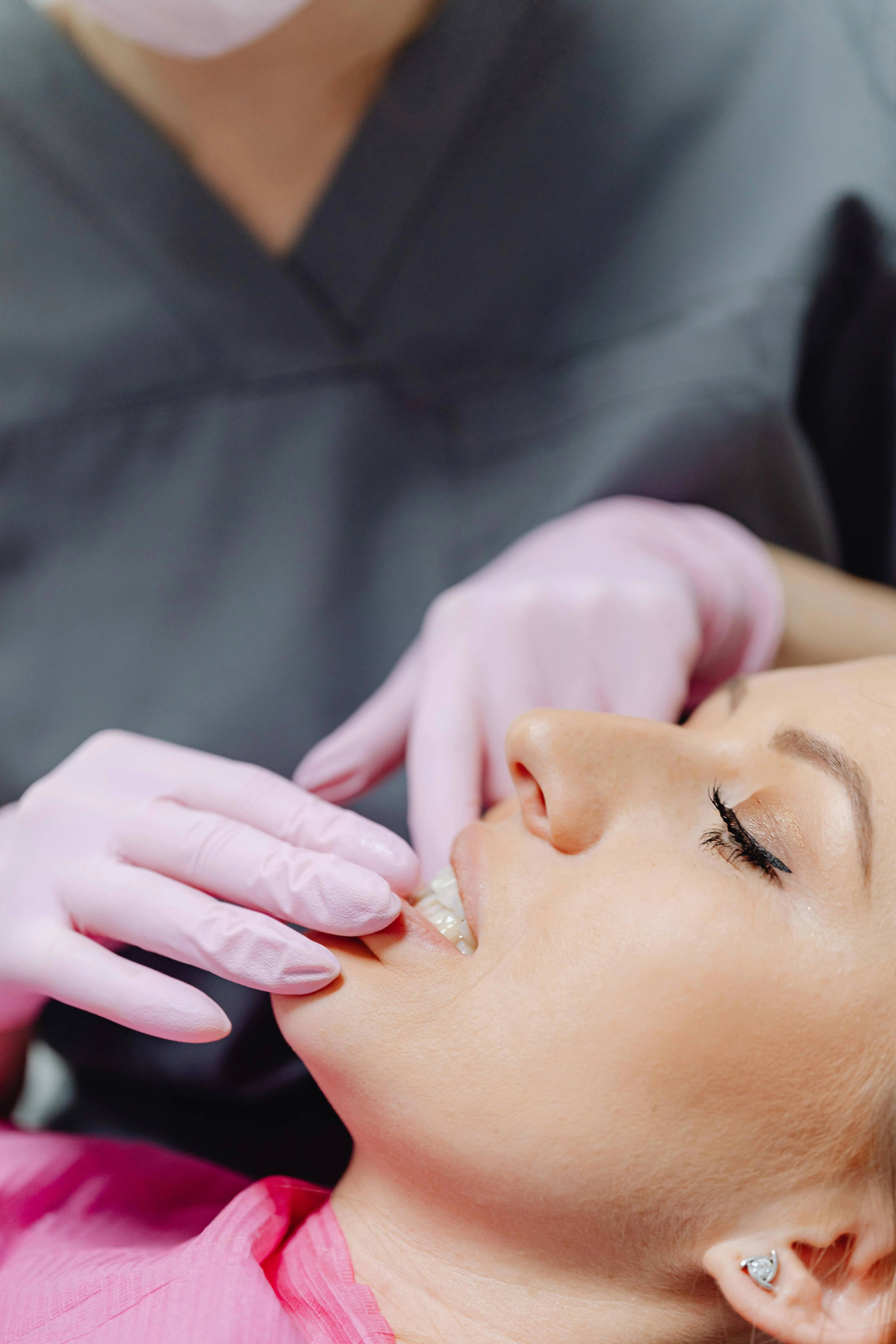 A stock photo of a woman having her teeth examined by a dentist wearing pink medical gloves