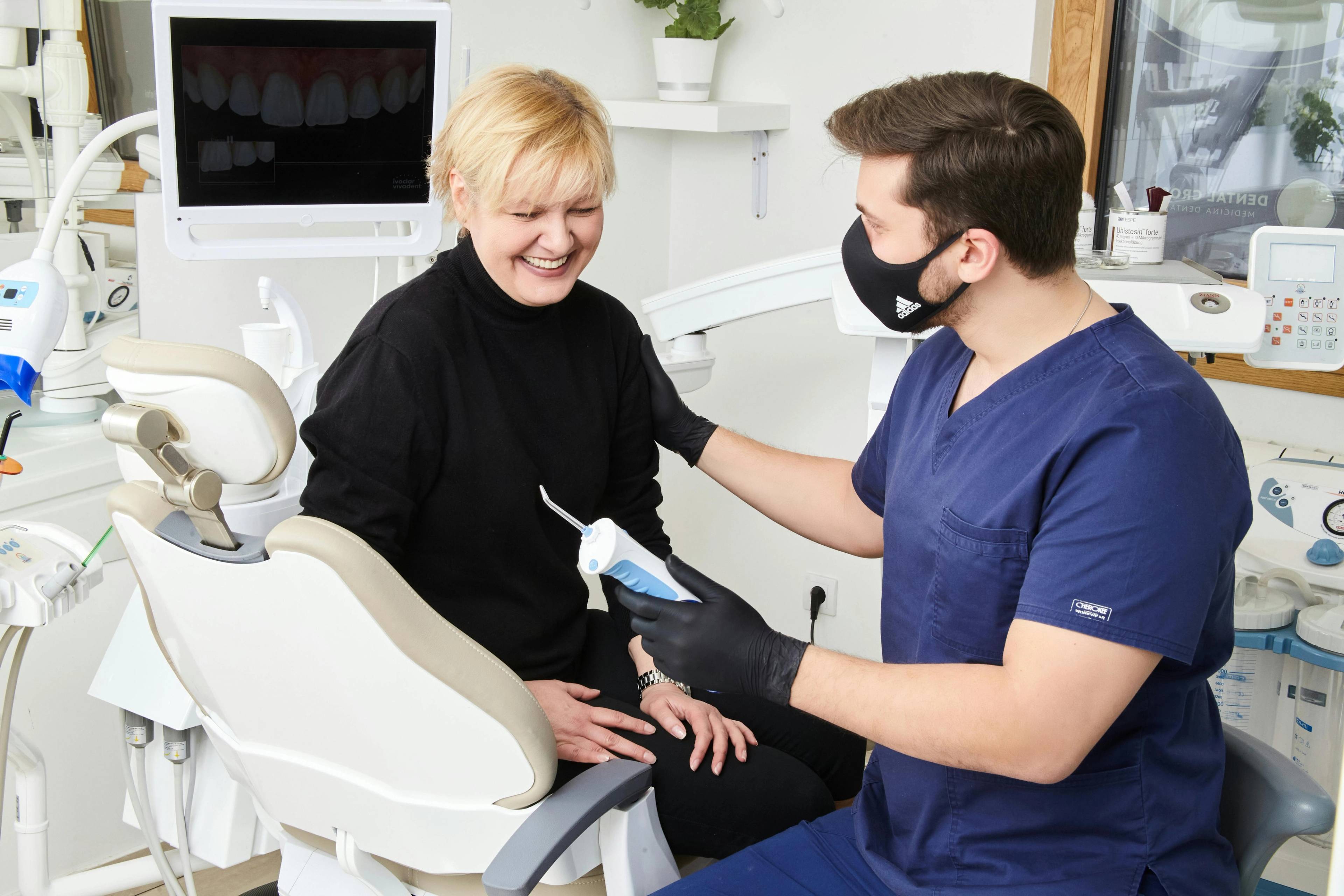 A stock photo of a patient being comforted by a dentist who is holding a teeth cleaning tool in a treatment room