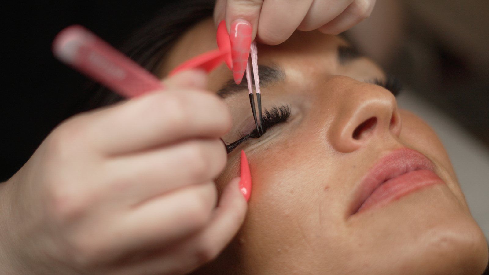 A lash artist placing an extension with fine tweezers while her client rests with eyes closed.