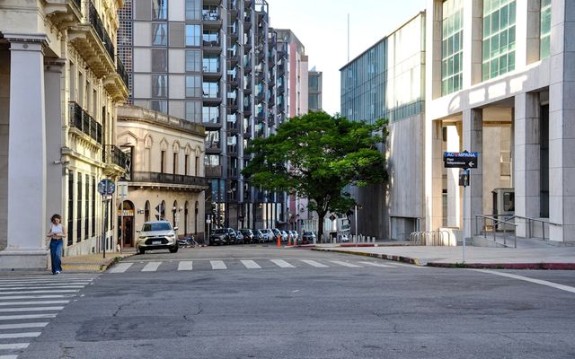 A person stands on a city street corner with buildings.
