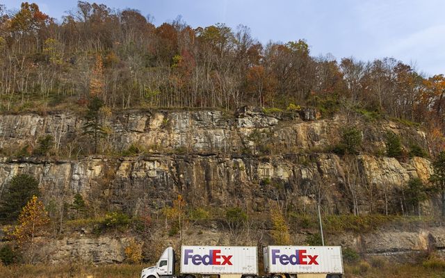 Fedex truck drives past a rocky cliffside in autumn.