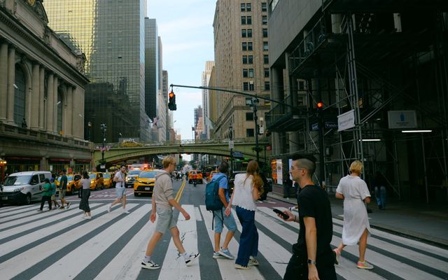 People crossing a busy city street with skyscrapers.
