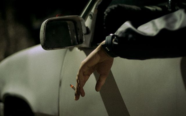 Person's hand holding cigarette out car window