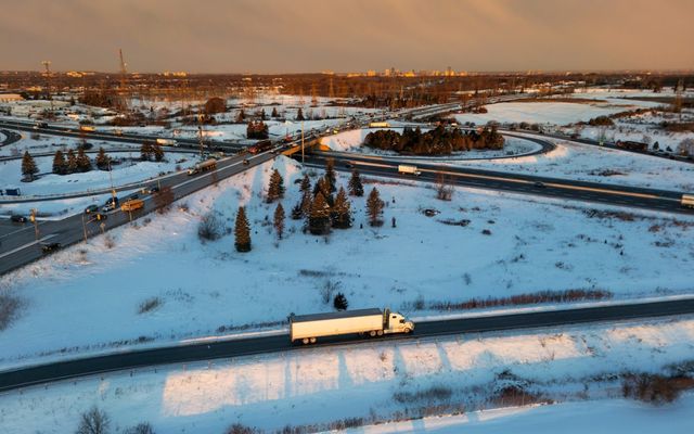 Semi-truck driving on a snowy highway at sunset.