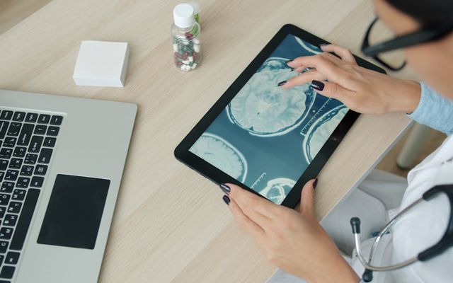 Doctor examining brain scan on tablet at desk.