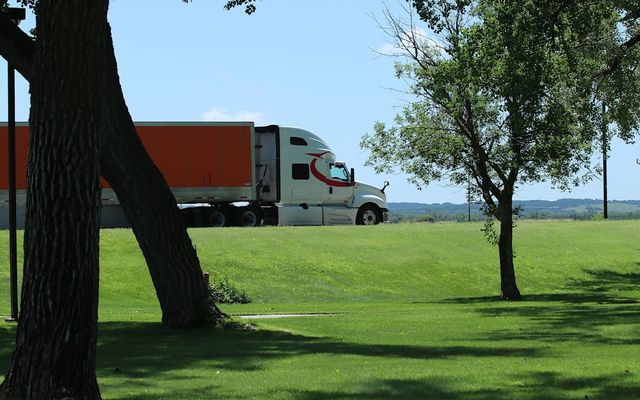 White semi-truck with orange trailer drives on road.
