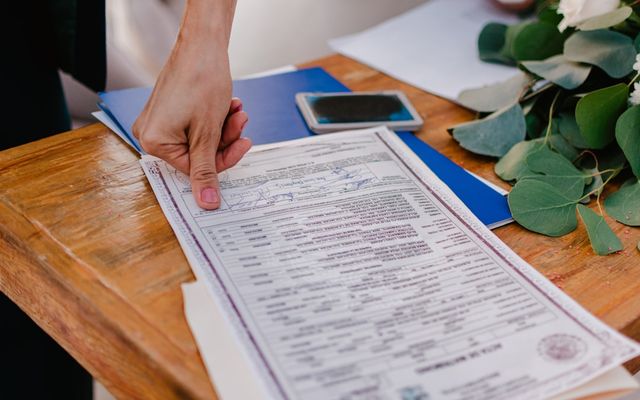Person pointing at a marriage certificate on a wooden table.