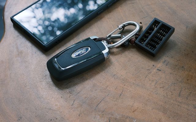 Car key, phone, and keychain on a wooden surface.