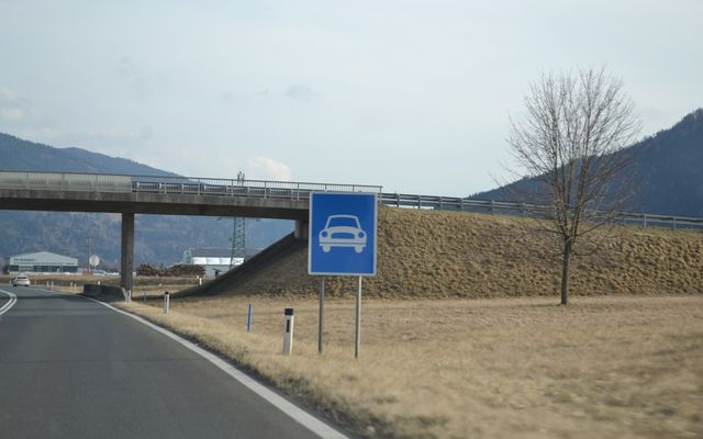 Blue sign with white car symbol near road
