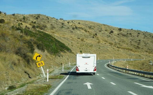 A white campervan drives on a winding road.