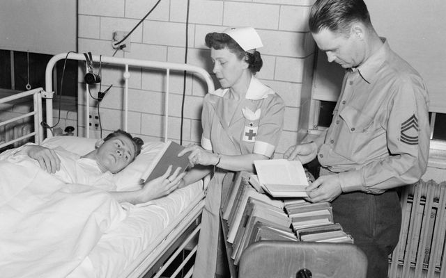Nurse and soldier give books to patient in hospital bed
