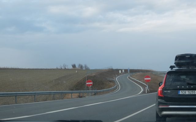 A car drives on a quiet highway under a cloudy sky.
