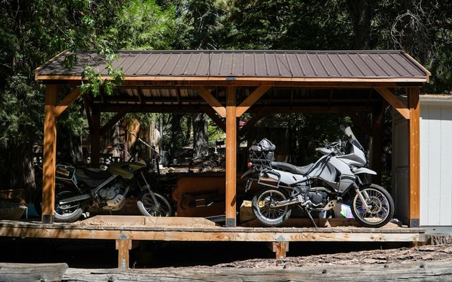 Two adventure motorcycles parked under a wooden shelter.