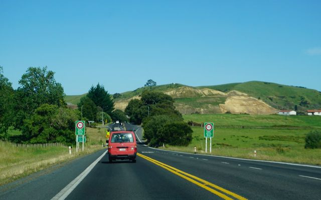 Red car driving on a highway through green hills.