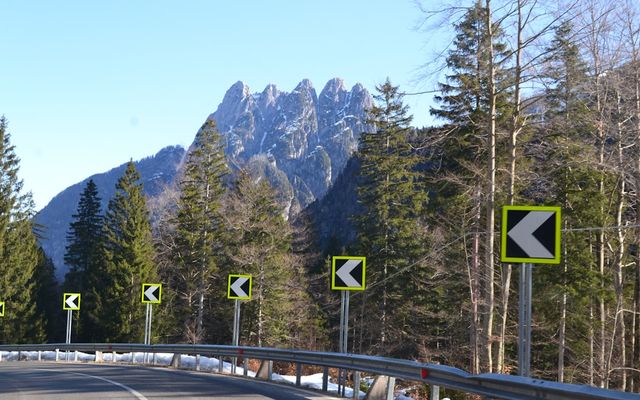 Roadside signs guide around a curve with mountains behind.