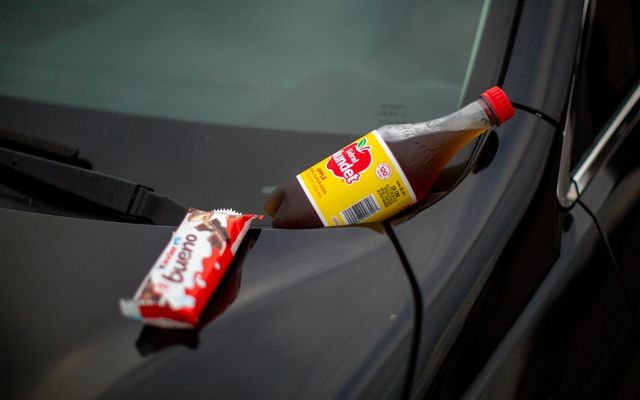 A bottle of soda sitting on the hood of a car