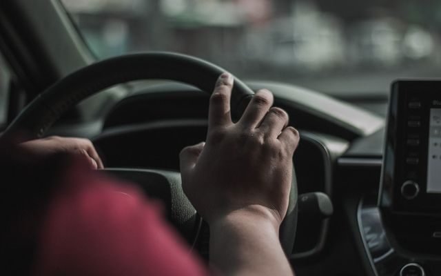 a person driving a car with their hand on the steering wheel