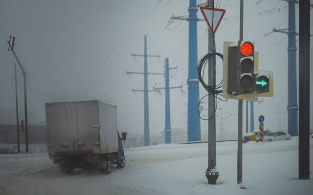 Truck driving in snowy weather with traffic lights.