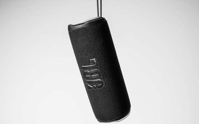 A black portable jbl speaker hanging against a white background.