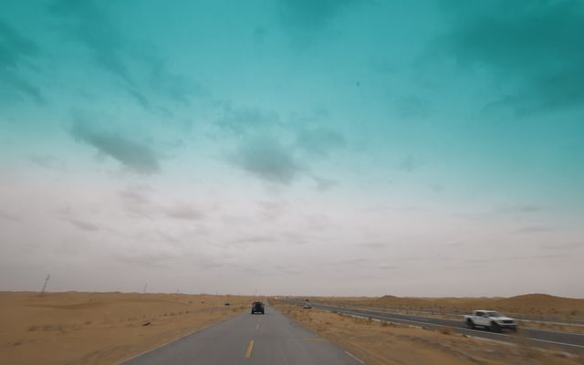 Cars driving on a desert road under a cloudy sky