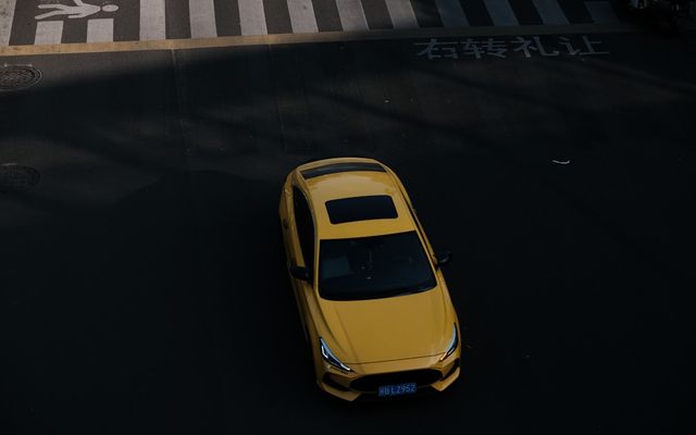 A yellow car drives on a street near a crosswalk.