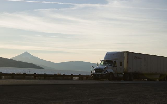 A semi-truck drives along a scenic highway near mountains.