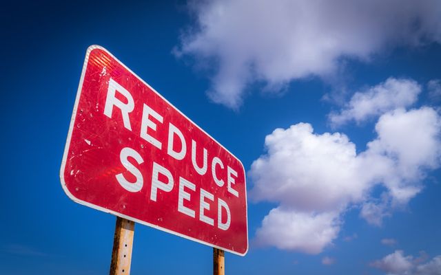 Red reduce speed sign against blue sky